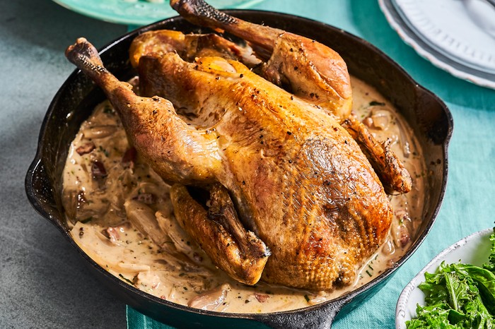 A black baking dish filled with a roast bird on a bed of creamy sauce