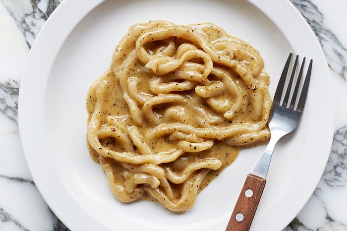 Padella's pasta pici cacio e pepe, with with a metal fork on a large white plate