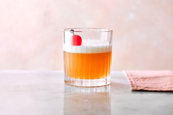 An amaretto sour in a tumbler topped with a cherry, with a napkin on the side