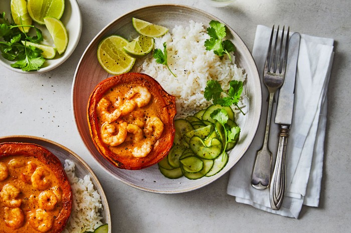 Two plates of rice, pickled cucumber and squash filled with prawn curry