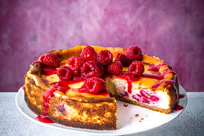 Baked raspberry cheesecake on stand, topped with raspberries