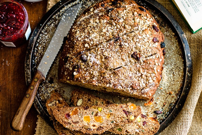 A large loaf of bread packed with oats, coconut, nuts and fruit, served on a round black plate