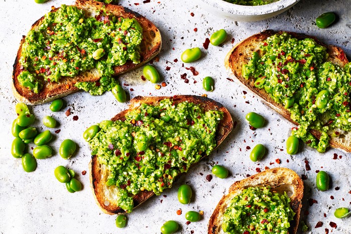 Several pieces of toast with smashed broad beans spread over them