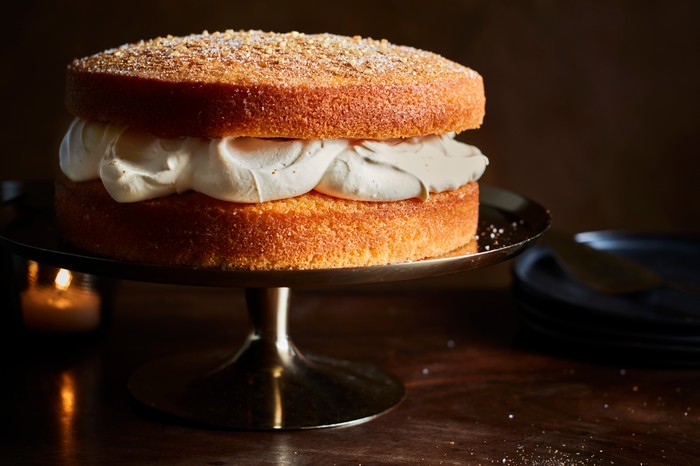 A sponge cake sandwiched with white cream on a cake stand with a mottled brown background