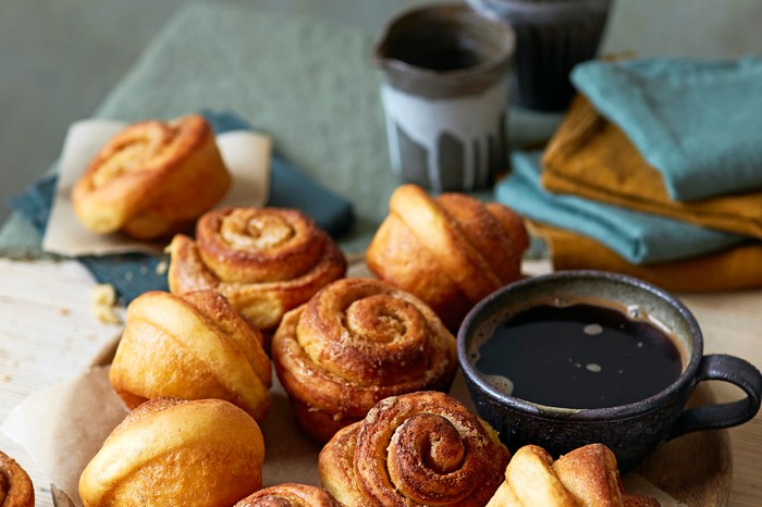 A wooden platter of cardamom buns with a mug of black coffee