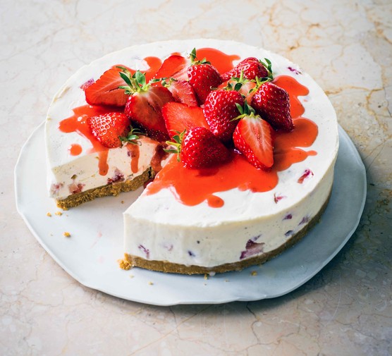A white cheesecake topped with red strawberries and whole strawberries on a white plate