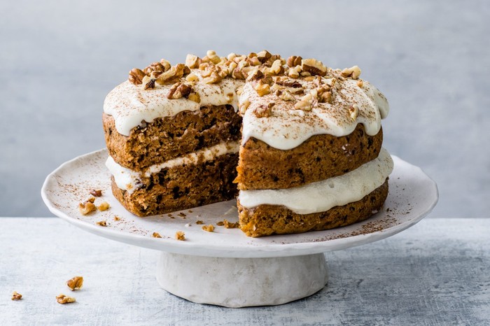 Vegan carrot cake topped with walnuts on a white cake stand