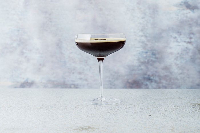 A martini glass filled with espresso martini on a grey background