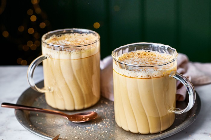 Two mugs filled with creamy eggnog latte, served on a metal tray