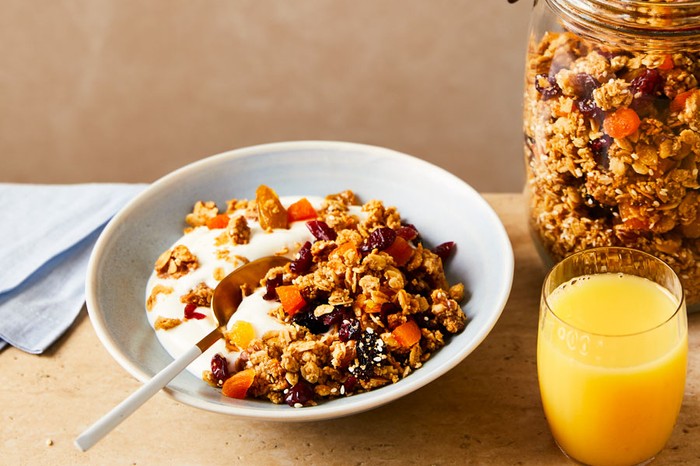 A bowl of granola next to a jar of granola and a glass of orange juice