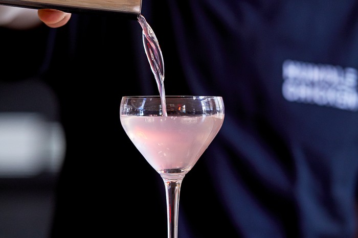 a pale pink liquid being poured into a martini glass from a copper cocktail shaker