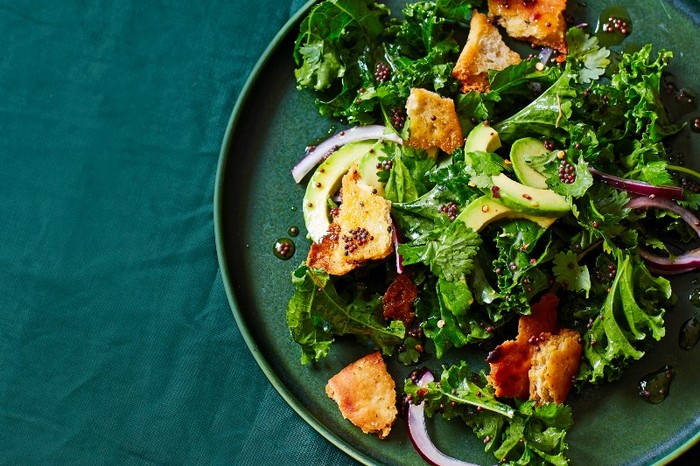 A green plate filled with kale, chopped avocado and golden croutons