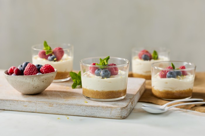 Four pots of mini cheesecakes topped with summer berries next to a small bowl of more berries