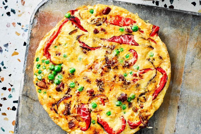 A chorizo frittata with red pepper and peas on a rustic baking tray