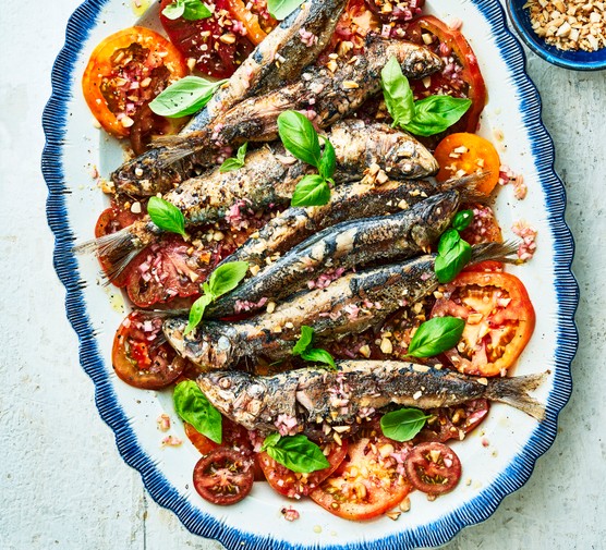 A white oval platter topped with slices of tomato and topped with grilled sardines