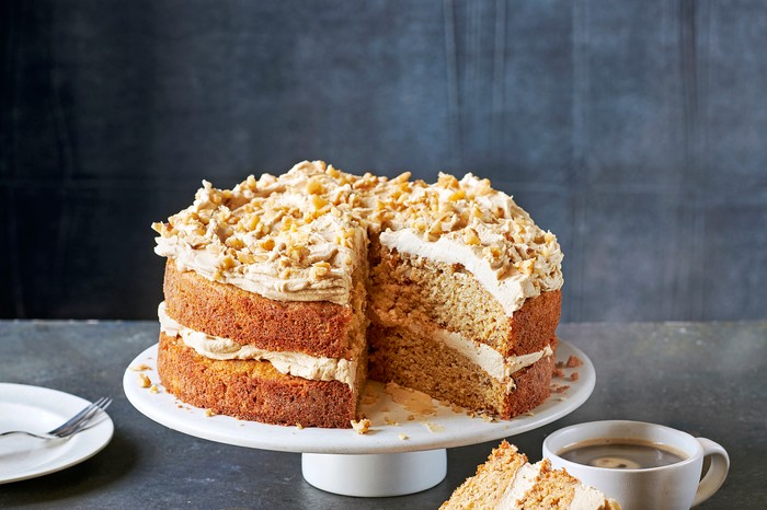 A white cake stand topped with a coffee and walnut sponge cake with a cream coffee icing
