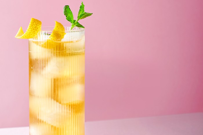 A classic whisky highball garnished with mint and lemon against a pink background