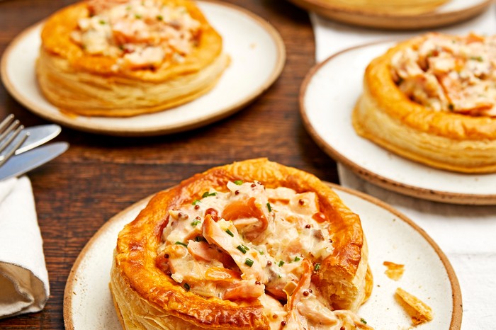Three white plates topped with golden puff pastry tarts filled with creamy smoked salmon