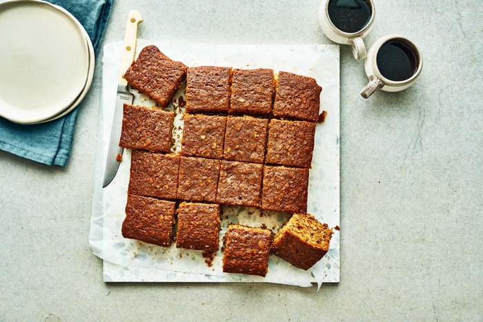 Ginger parkin on baking paper, two cups of coffee, a white plate and kitchen knife