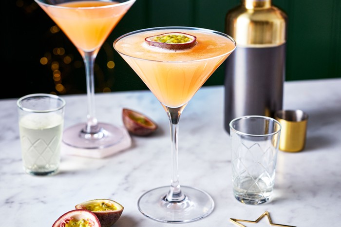 Two martini glasses filled with passion fruit martini, topped with passion fruit half