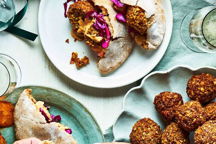 A table spread with plates piled high with falafels, pitas bread, red cabbage salads