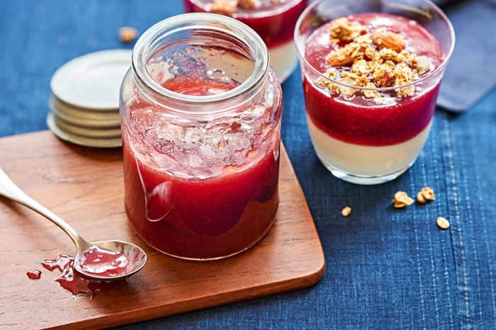 Jar of plum compote next to a glass of yogurt and compote topped with nuts