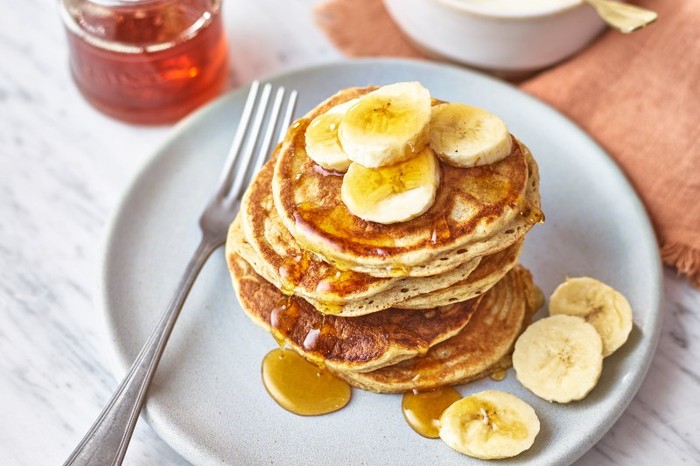 A stack of protein pancakes topped with slices of banana and honey on a white plate