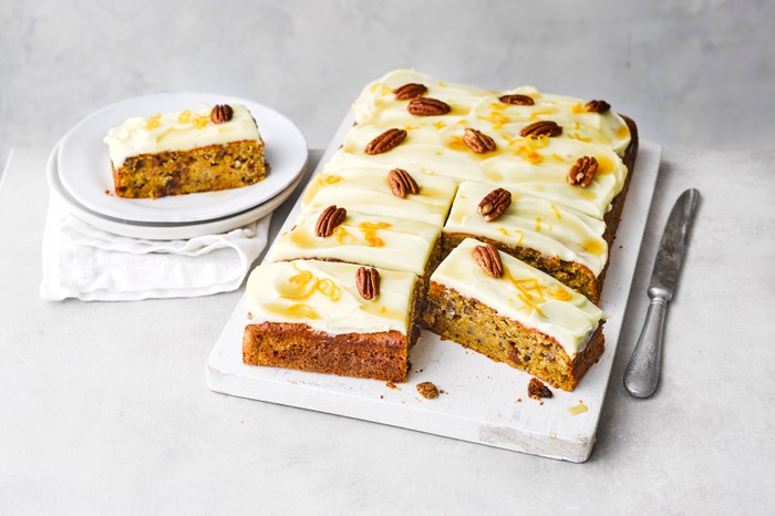 Pumpkin cake cut into squares and served on a white serving board, next to a small plate with a slice on top