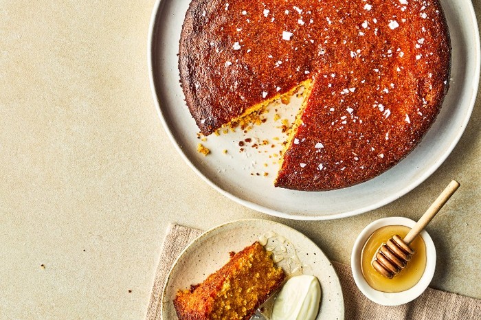 a golden-topped cake with flakes of salt next to a small bowl of honey and little pot of salt