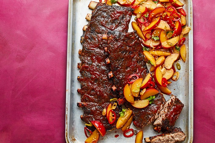 Baby back ribs covered in plum sauce next to a plum salad on a baking tray.