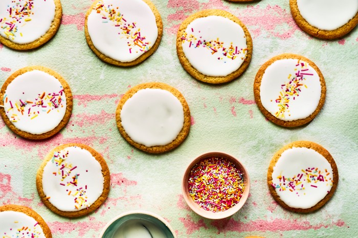 Circular biscuits topped with white icing and multicoloured sprinkles on a textured green background