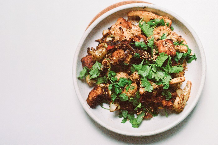 A white plate with a tofu stir-fry on it, topped with coriander