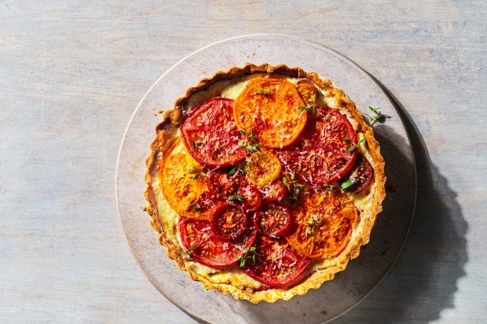 A tomato tart on a round plate with a grey wood background