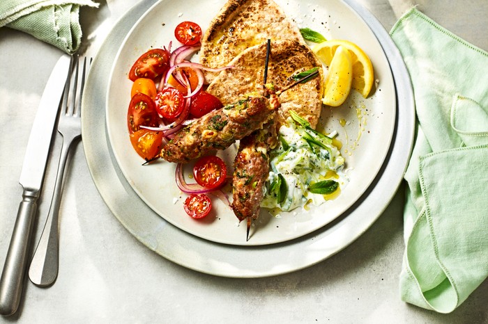 A plate on a white background with green napkins, filled with turkey skewers and charred pitta breads
