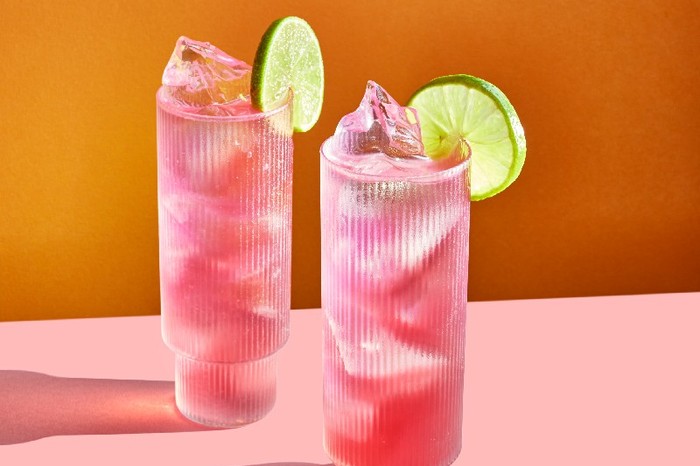 Two pink cocktails in tall glasses garnished with a slice of lime