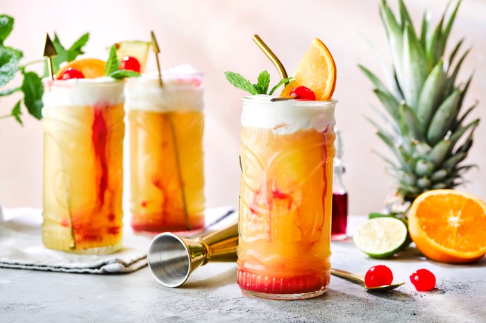 Three tall zombie cocktails with fruit in the background