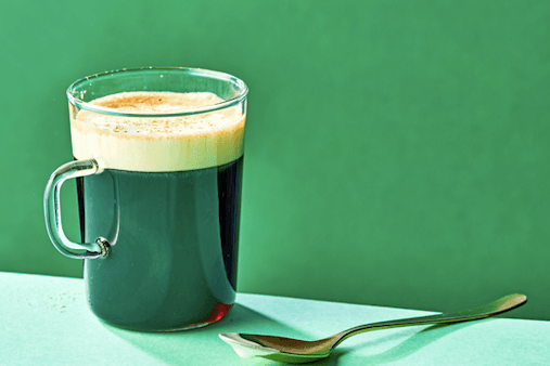 A glass of Irish coffee with a brass spoon on a green background